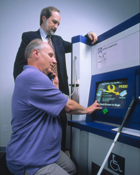 A photograph of Neal Ewers and Dr. Gregg Vanderheiden testing an accessible kiosk.