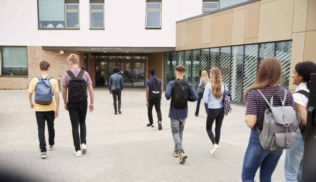 group of teenagers with backpacks walking into school
